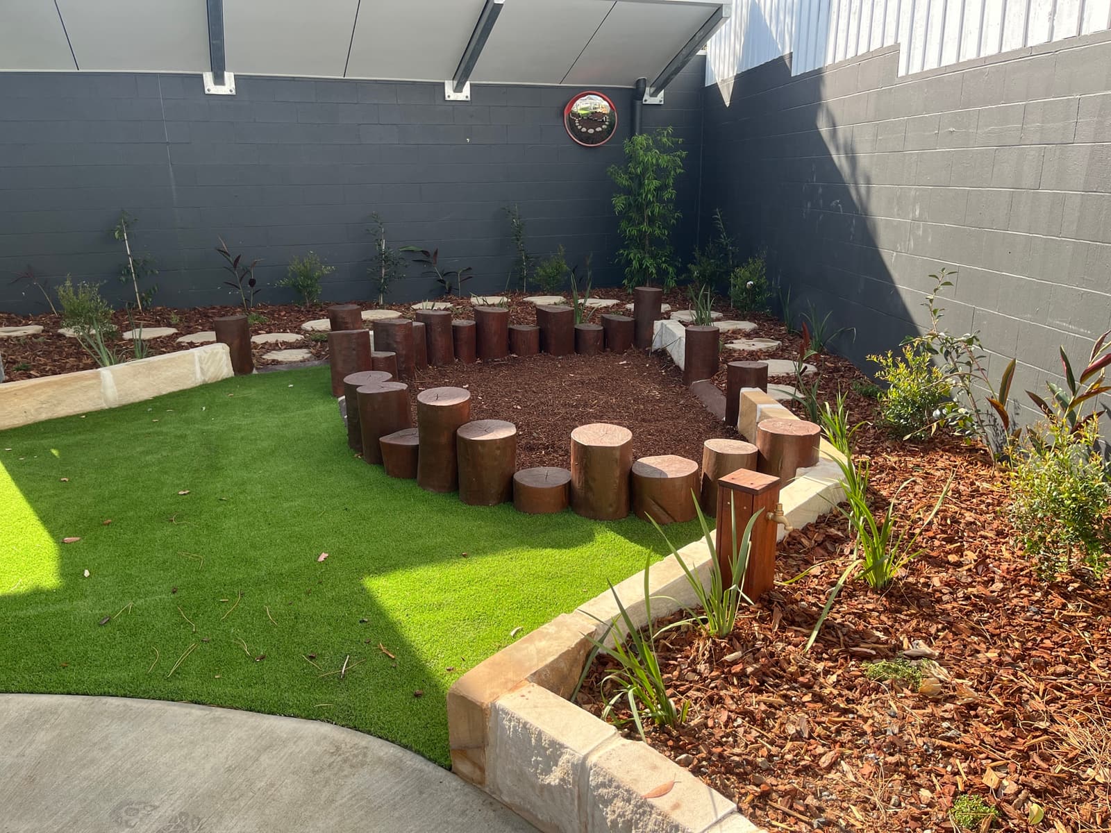 Spiral of timber log steppers in a mulched garden corner with sandstone edging and synthetic turf in the foreground in Cooranbong