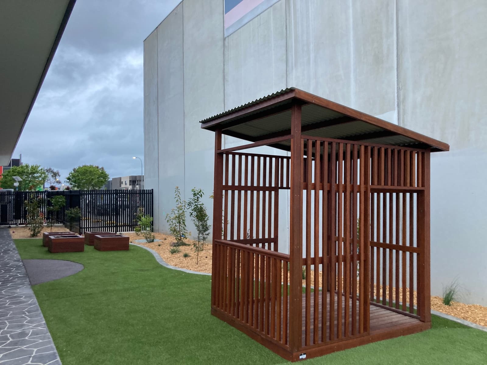 Slatted timber cubby with a metal skillion roof on synthetic turf, with raised planter boxes behind, in Cranbourne