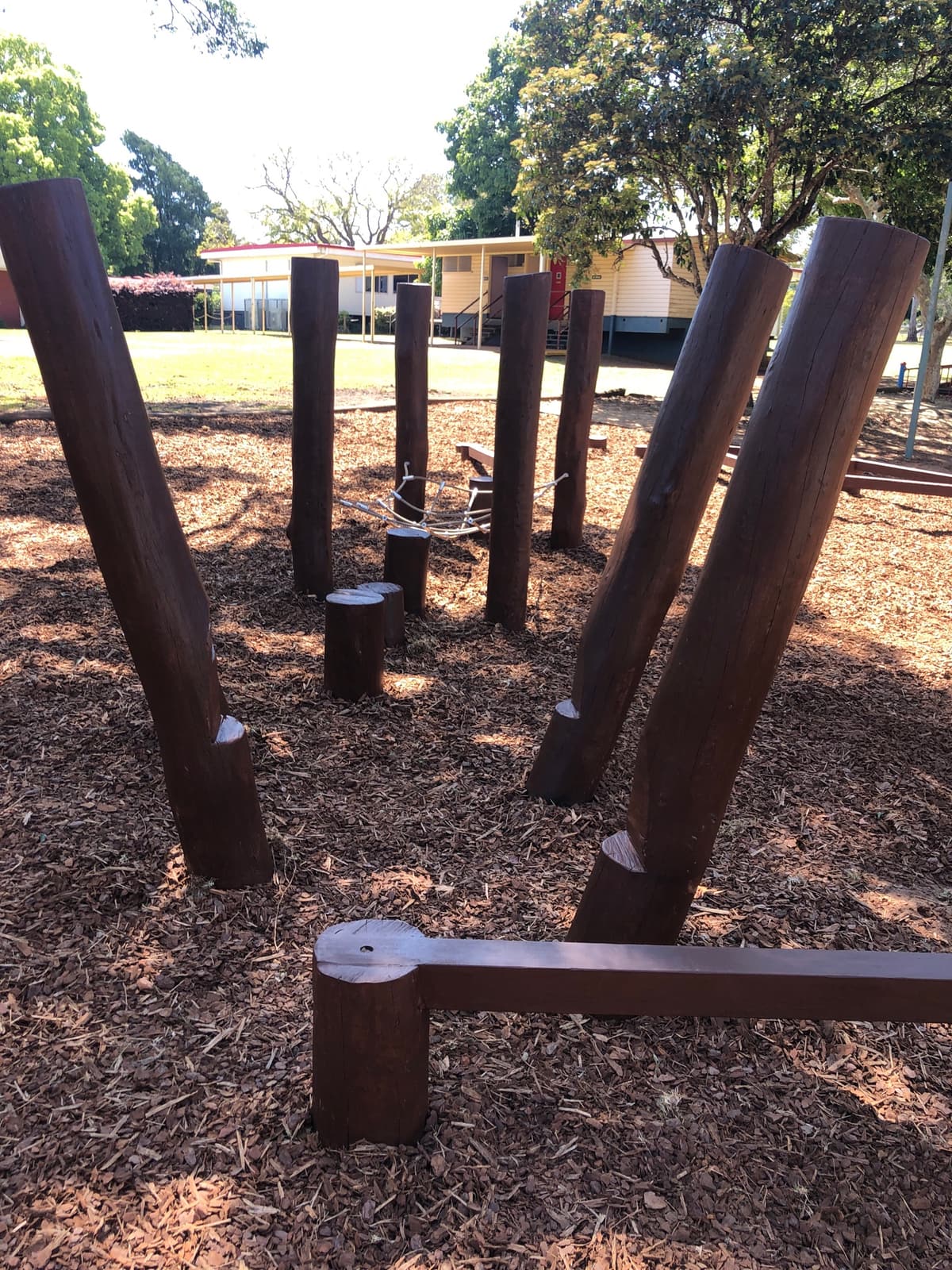 Upright and angled round timber posts with log steppers and low balance beams on bark mulch in Highfields